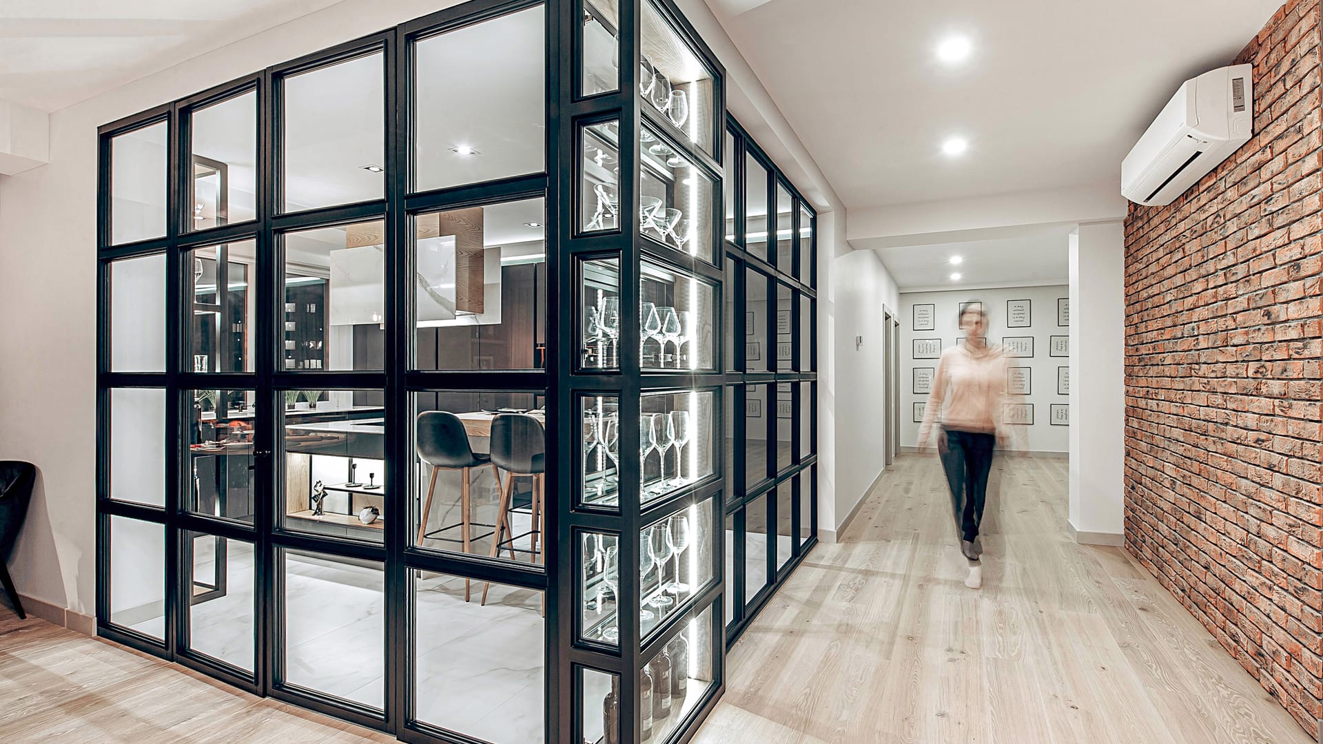 View from the hallway: glass display cabinet for glassware and wine, a brick wall and the kitchen's steel partition