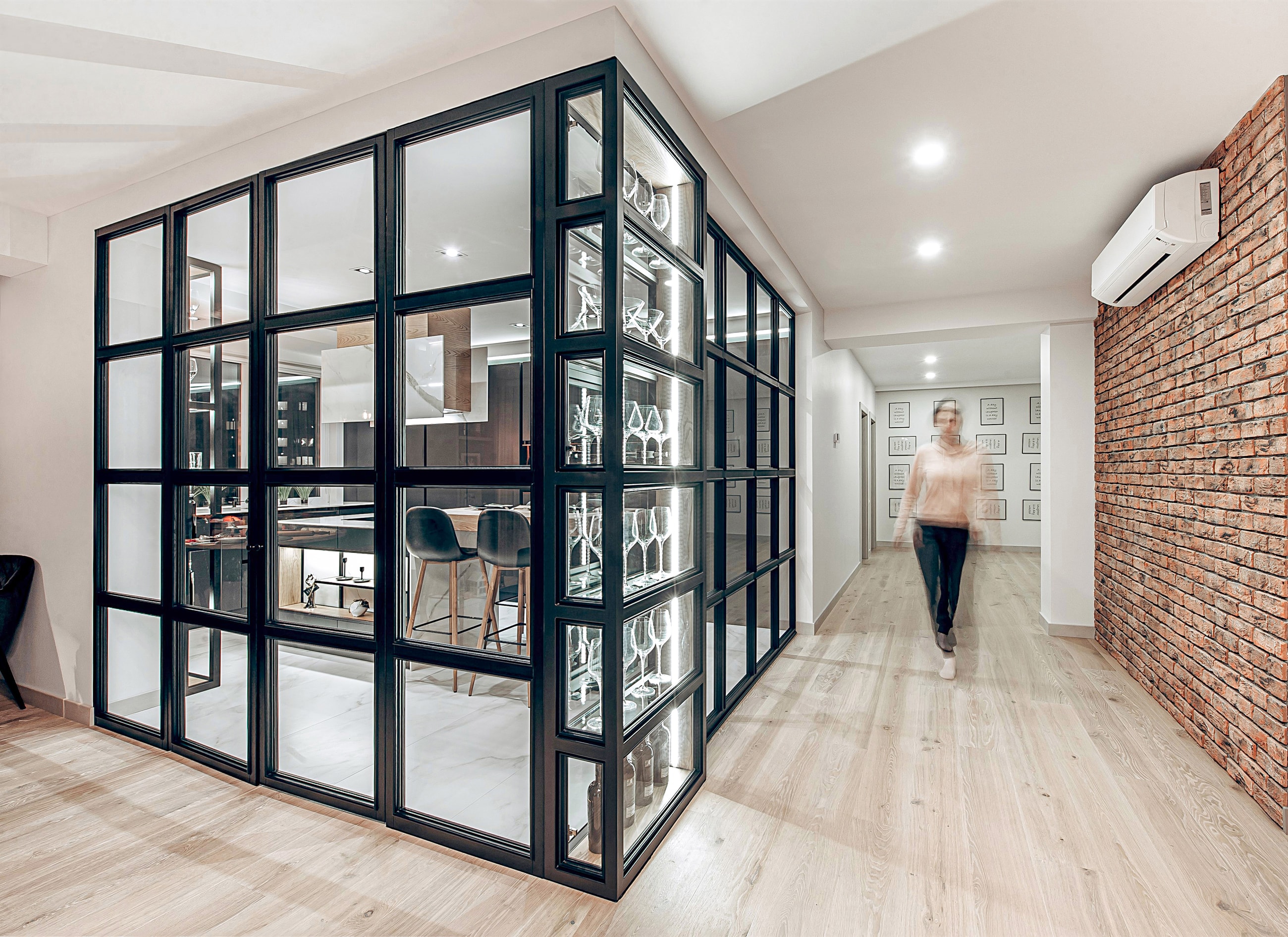 View from the hallway: glass display cabinet for glassware and wine, a brick wall and the kitchen's steel partition