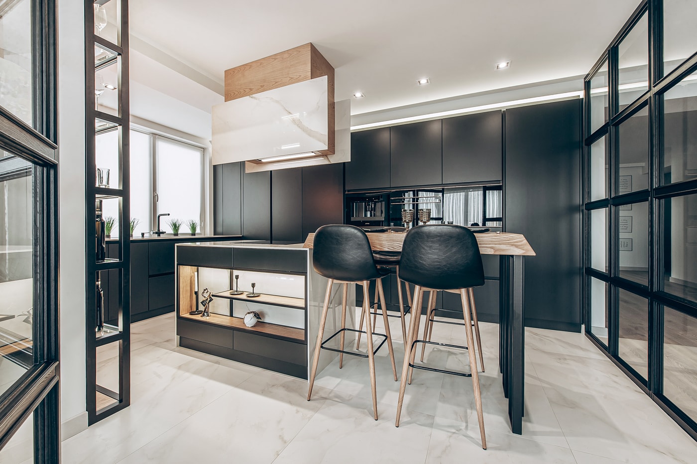 Island clad in marble with an oak breakfast bar, black stools and an extractor in marble and oak