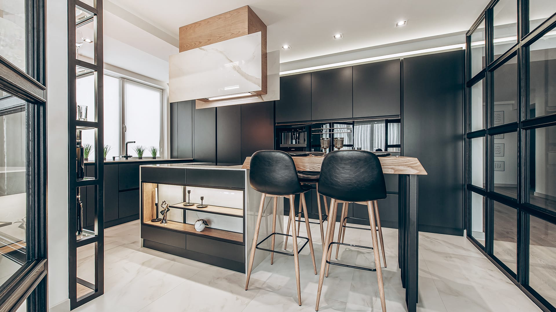 Island clad in marble with an oak breakfast bar, black stools and an extractor in marble and oak