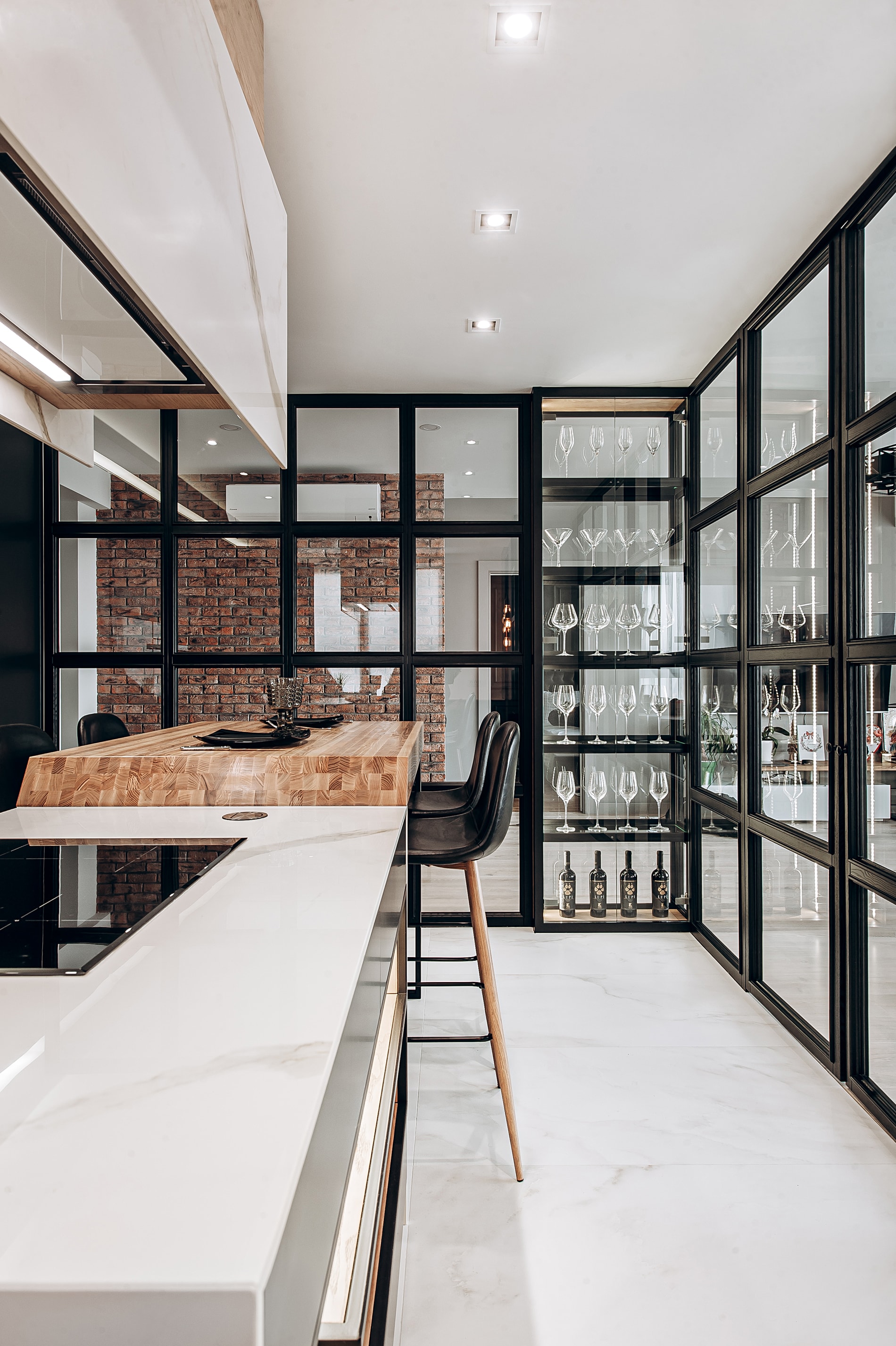 The completed kitchen space: a marble island, oak bar, glass wine display and a black steel partition