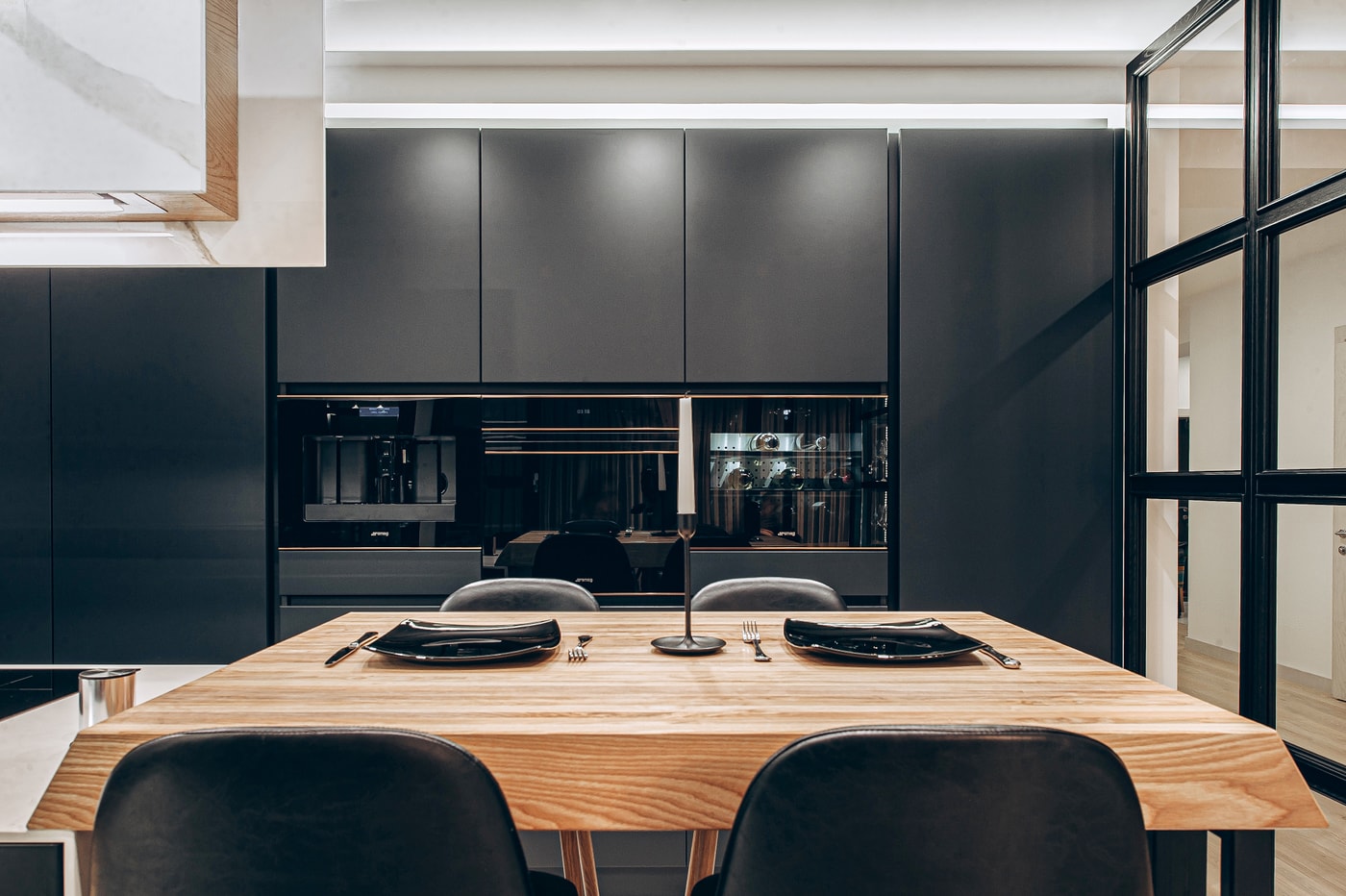 Oak dining table opposite the appliance run: coffee machine, oven and wine cooler in black cabinetry